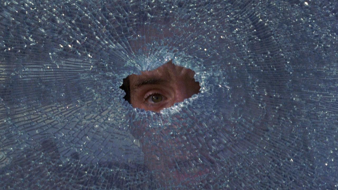 still from To Live and Die in L.A. (1985) - a frightened man stares out from a central bullet hole in a splintered car windshield
